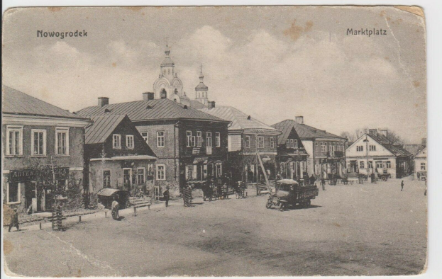 Schwarz-weiß-Fotografie einer Stadtstraße in Nowogrodziec, Deutschland, mit Gebäuden, Menschen, Karren, Pfählen, Bäumen und Himmel, mit der Aufschrift "Marktplatz in Nowogrodeek, Deutschland" oben und unten.