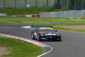 Ein schwarzer Sportwagen auf einer Rennstrecke umgeben von Gras, Verkehrskegeln, Absperrungen und Bäumen.