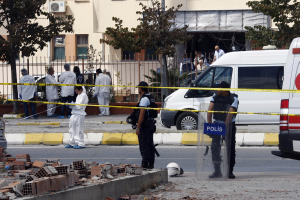 Eine Gruppe von Polizisten steht vor einem Gebäude mit Fenstern, umgeben von Fahrzeugen, einem Zaun, Bäumen und Pflanzen, mit Ziegelsteinen und einem Helm auf dem Boden, wahrscheinlich nach einer Bombenexplosion in Mexiko-Stadt.