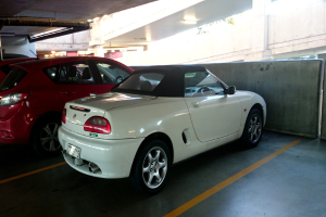 Autos sind in einem Keller mit einem Rohr am Dach und einem weiteren Geb├Ąude oben rechts geparkt.