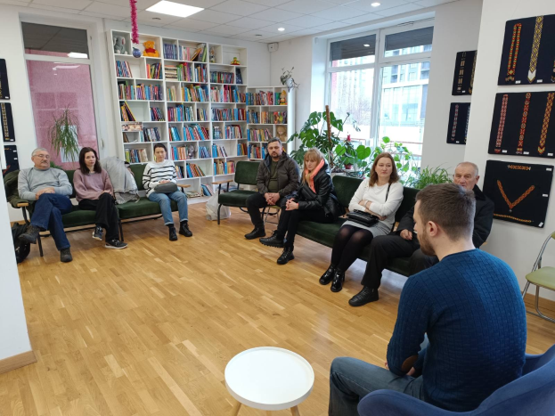 Eine Gruppe von Menschen sitzt um einen Tisch in einem Raum mit Bücherregalen, Pflanzen und einem Fenster, die während einer Workshop-Diskussion über die Zukunft von Gesundheit und Wohlbefinden in Berlin, Deutschland, diskutieren.