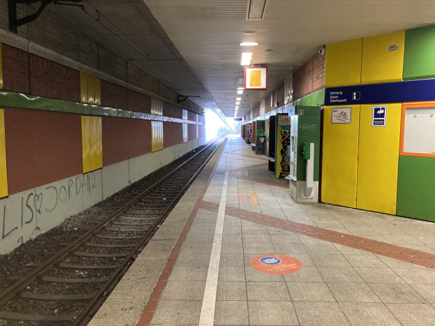 Ein Bahnsteig mit einem auf den Schienen stehenden Zug, beleuchtet von Deckenlampen, mit Graffiti an der linken Wand und einigen Gegenständen auf der rechten Seite, identifiziert als Berlin Hauptbahnhof in Berlin, Deutschland.