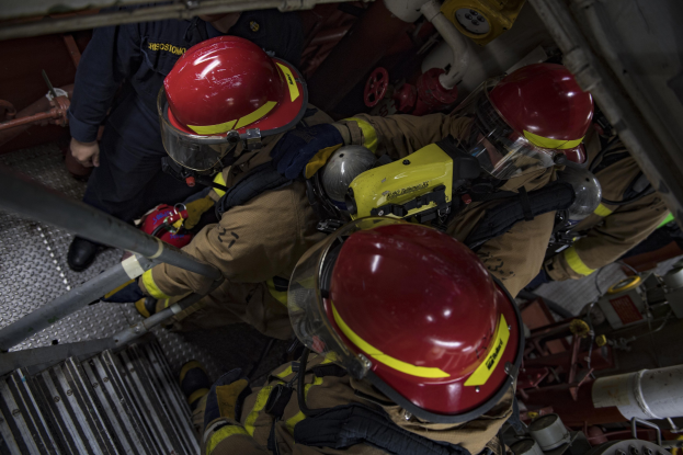 Feuerwehrleute in Schutzausrüstung bei der Arbeit an einem Feuerlöschfahrzeug mit Equipment im Hintergrund.