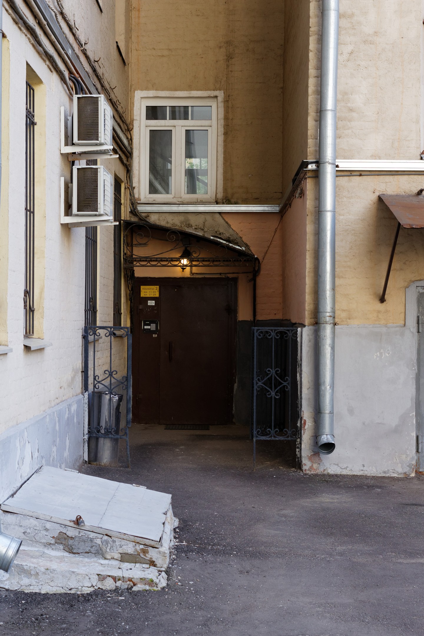 Gasse mit einem Geb├Ąude mit einer Tür, Fenstern, Klimaanlagen, einem Metalltor, einer Lampe, einem Rohr und einem Dach über einer Stra├če.