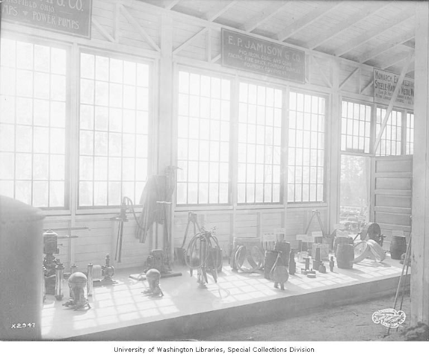 Schwarz-weiß-Foto eines großen Raums voller Werkzeuge, Maschinen und Tafeln mit Text an den Wänden, beschriftet mit "P.J. Jamison & Co. Power Pumps".