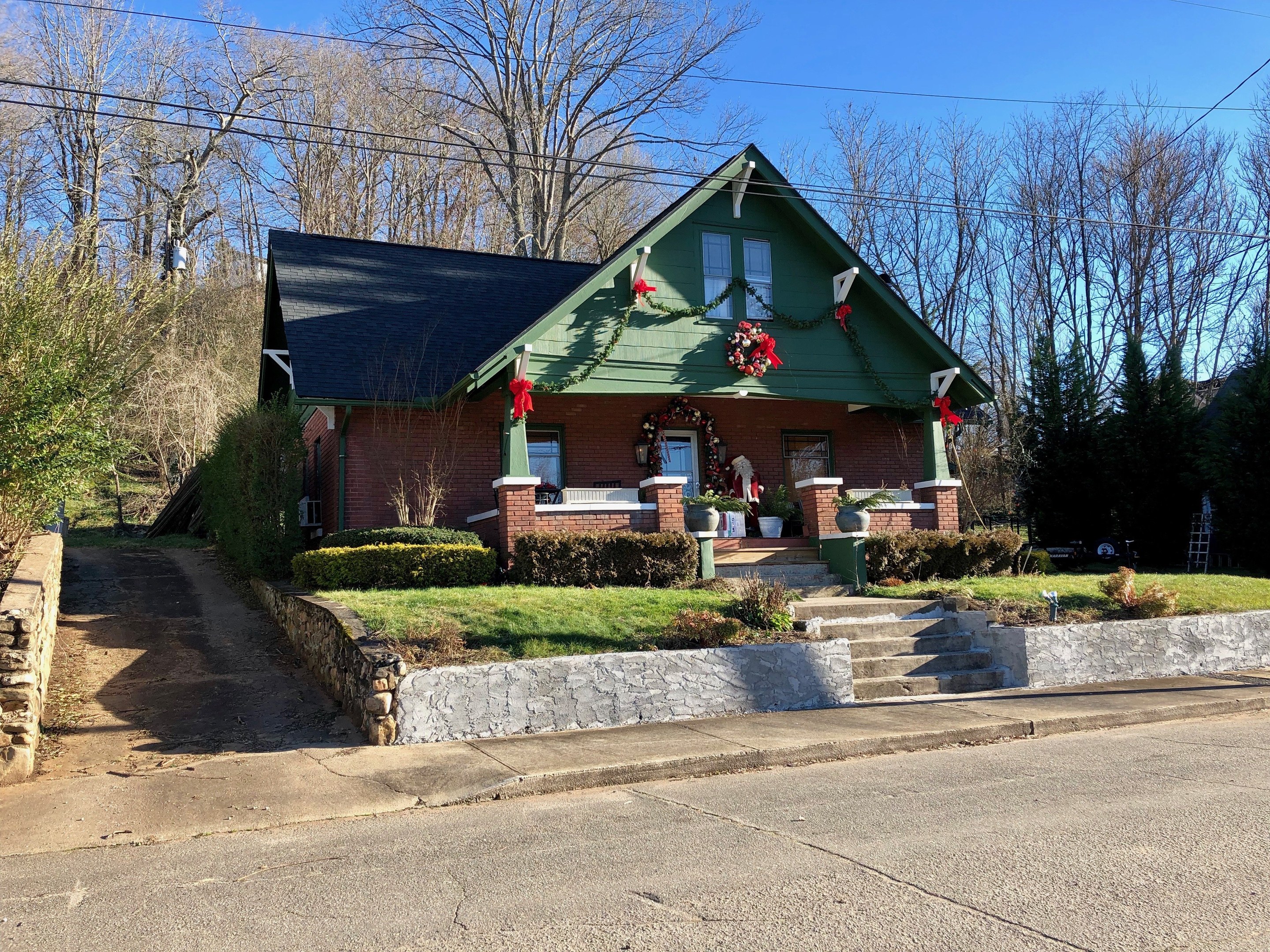 Ein grünes Haus mit einem Kranz an der Vorderseite, umgeben von Pflanzen, Gras, Treppen, einer Wand, Bäumen, Drähten und einem bewölkten Himmel, das sich in der Stadt befindet und zur Miete verfügbar ist.