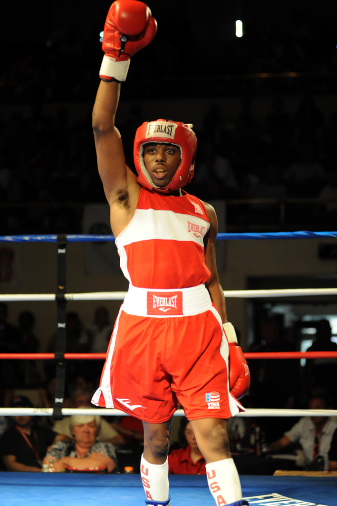 Ein Mann in Boxer-Ausrüstung, einschließlich Helm und Handschuhen, steht in einem Boxring mit Zuschauern im Hintergrund.