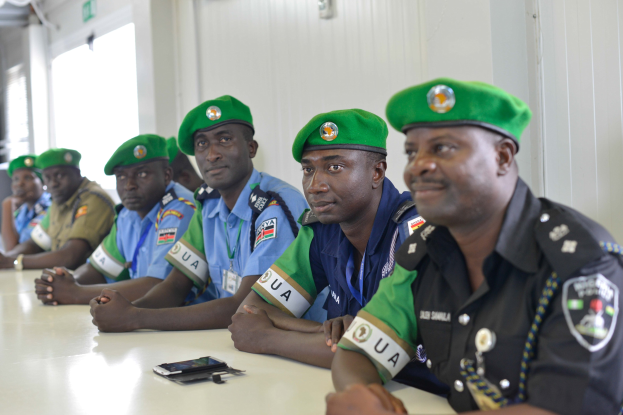 Gruppe von Polizeibeamten bei einer Schulung an einem Tisch sitzend, mit Mobiltelefonen und anderen Gegenständen auf dem Tisch, in einem Raum mit Fenstern und Deckenbeleuchtung.