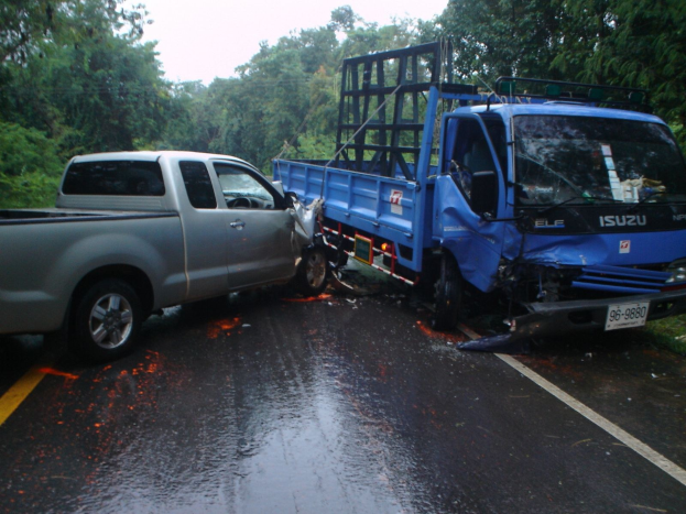 Ein schwer beschädigtter Lkw mit eingedellter Front und verbeulter Karosserie liegt am Straßenrand, umgeben von Bäumen unter einem klaren blauen Himmel.