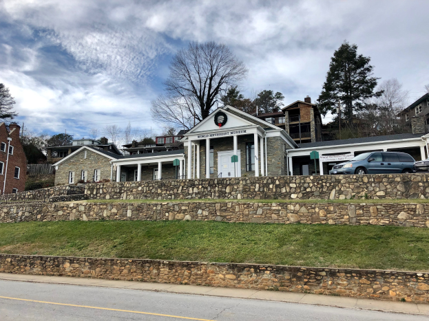 Steinmauer mit geparkten Autos, angrenzende Gebäude mit Fenstern und Türen, Bäume und ein bewölkter Himmel, als Weltkulturerbe-Museum identifiziert.
