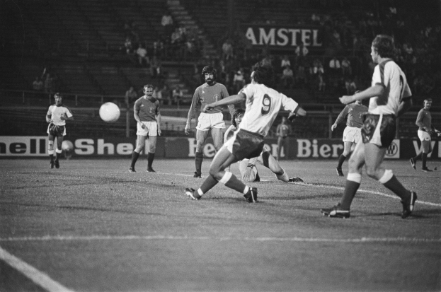 Schwarzes Foto von Männern, die Fußball in einem Stadion mit Zuschauern im Hintergrund spielen.